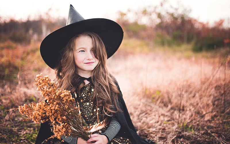 دختربچه ای با کلاه جادوگری و دسته گلی خشکیده در دست