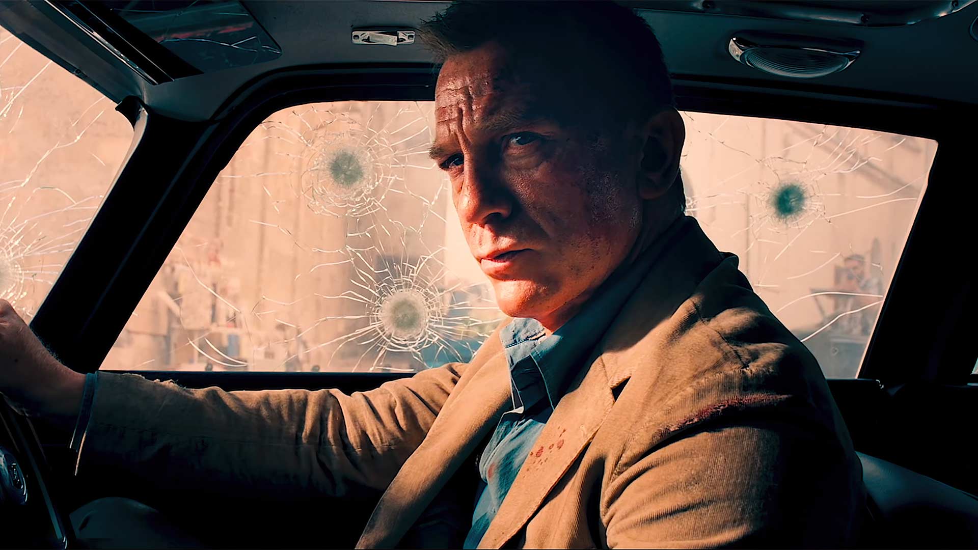 دنیل کریگ در نقش جیمز باند در ماشین استون مارتین که به گلوله بسته شده در فیلم No Time To Die